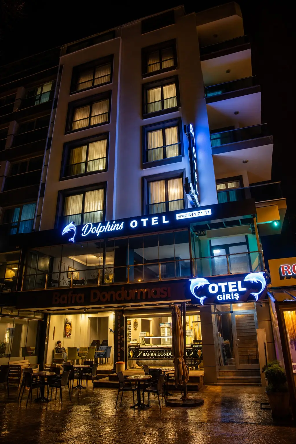 Das Hotel bei Nacht: das beleuchtete Schild „Dolphins Otel“ an der Fassade und der Eingang