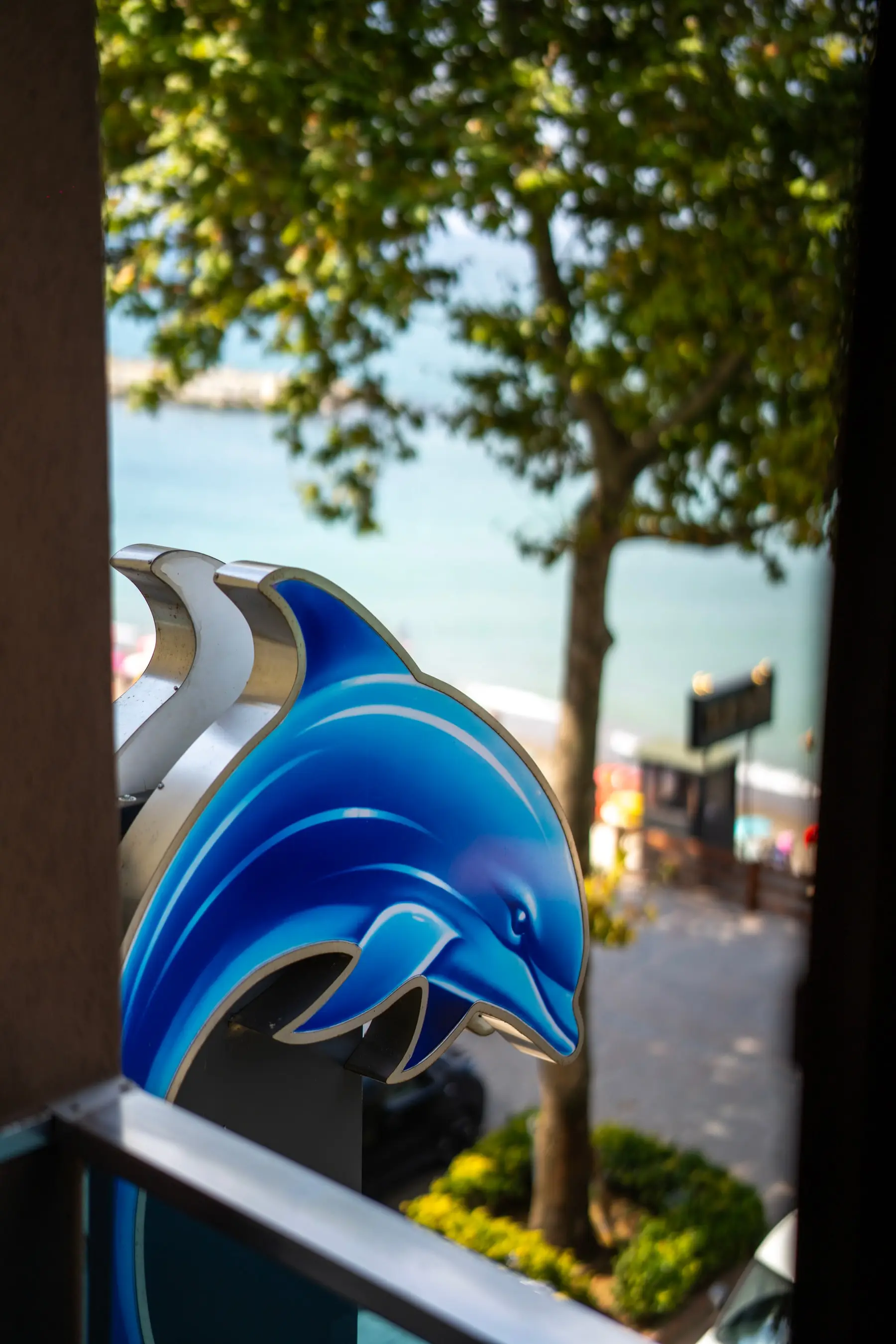 Die Delfinfigur am Schild, dahinter die Uferstraße und das Schwarze Meer